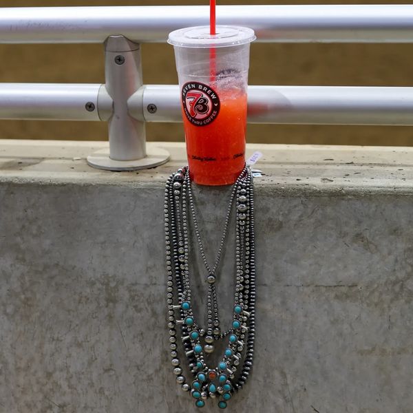 Iced red drink with a red straw on a concrete ledge, adorned with a beaded necklace.