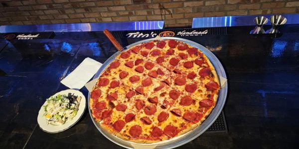 Large pepperoni pizza with a side salad on a dark table.