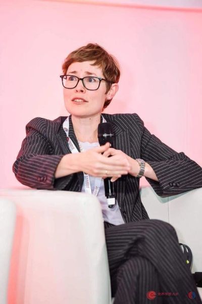 Woman in pinstripe suit speaking with a microphone at an event.