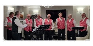 A group of men singing in matching red vests indoors.
