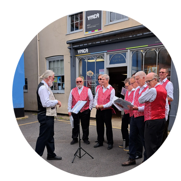 A group of elderly men in red vests singing outdoors with a conductor.