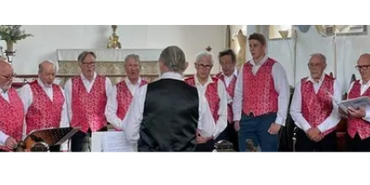 A men's choir dressed in red vests performs indoors.
