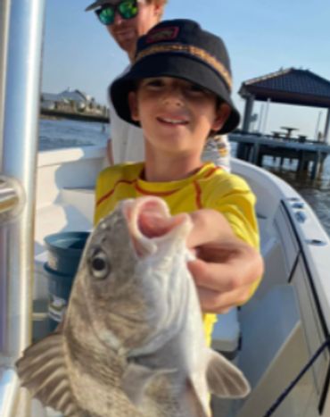 A boy proudly holding a freshly caught fish on a boat.