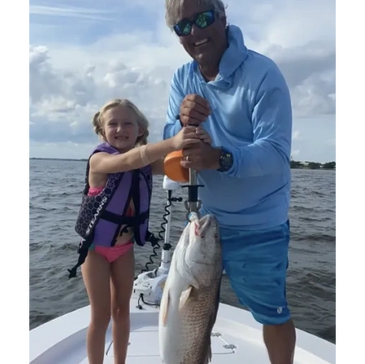 A man and a young girl proudly hold a large fish on a boat.
