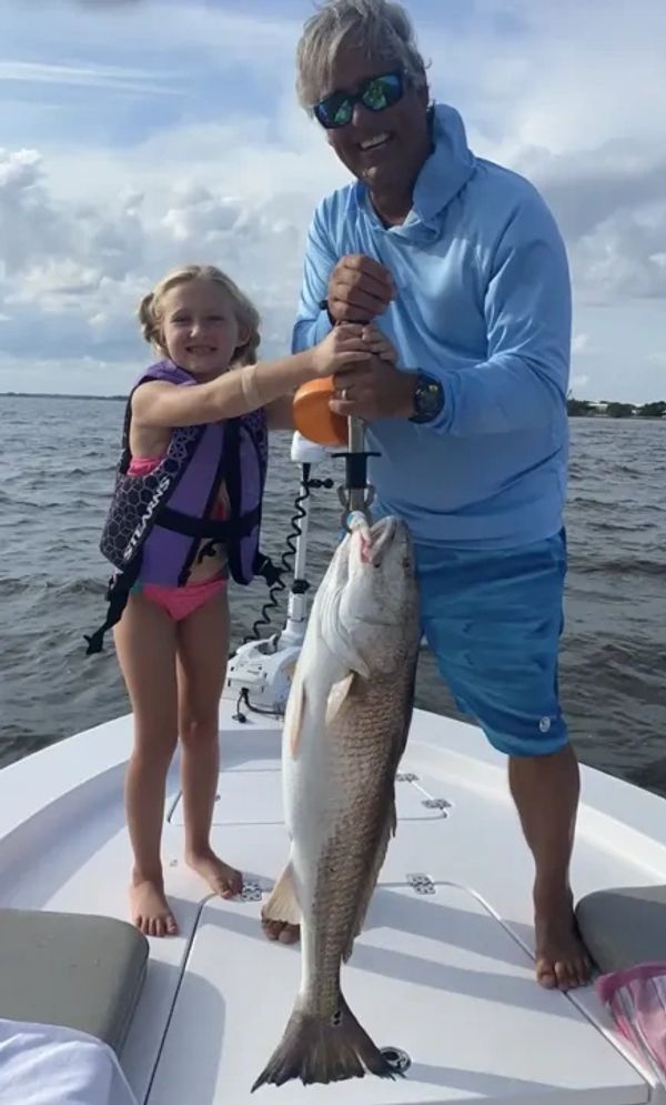 A man and a girl proudly hold a large fish on a boat.