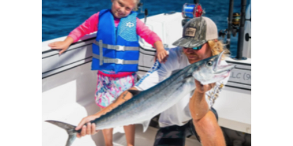 Man and child on a boat holding a large fish they caught.