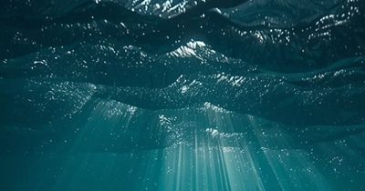 Sunlight piercing through ocean waves underwater.