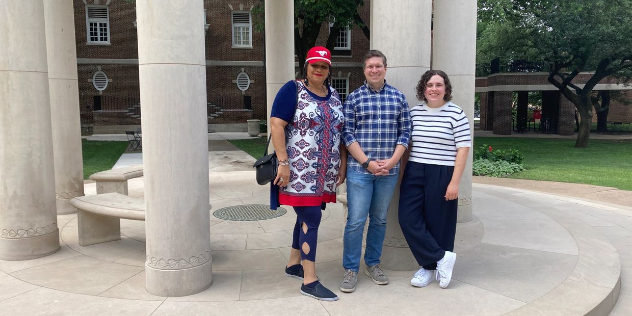 Three people standing together in front of large columns outdoors.