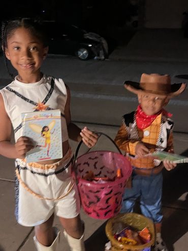 Children smiling in their costumes as they choose free books — a joyful moment from our Trick-or-Tre