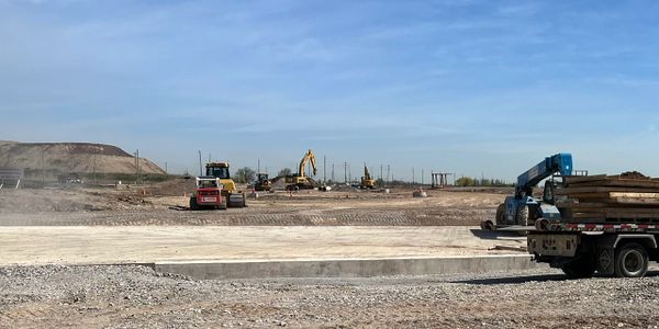 Construction site with heavy machinery working on land clearing under a blue sky.