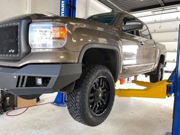 A lifted brown pickup truck on a hydraulic lift in a garage.