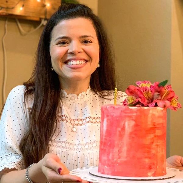 Woman smiling while holding a pink cake with flowers on top.