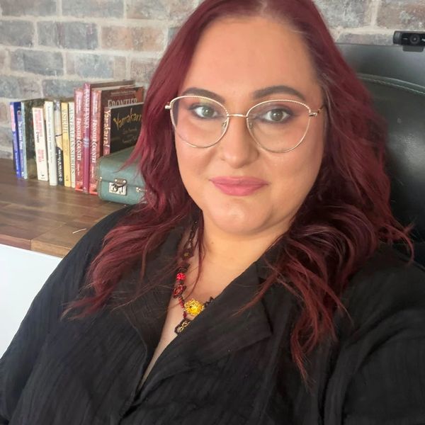 Smiling woman with glasses and red hair in a cozy room.