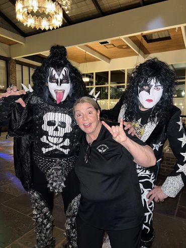 Two people in KISS band costumes pose with a smiling woman making a rock hand sign.