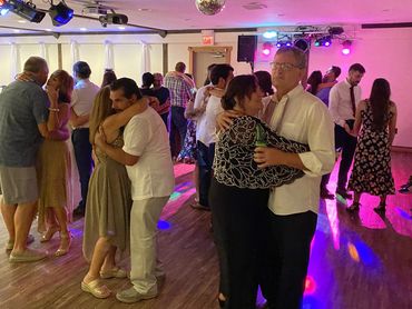 Couples slow dancing in a warmly lit room with colorful party lights and a disco ball.