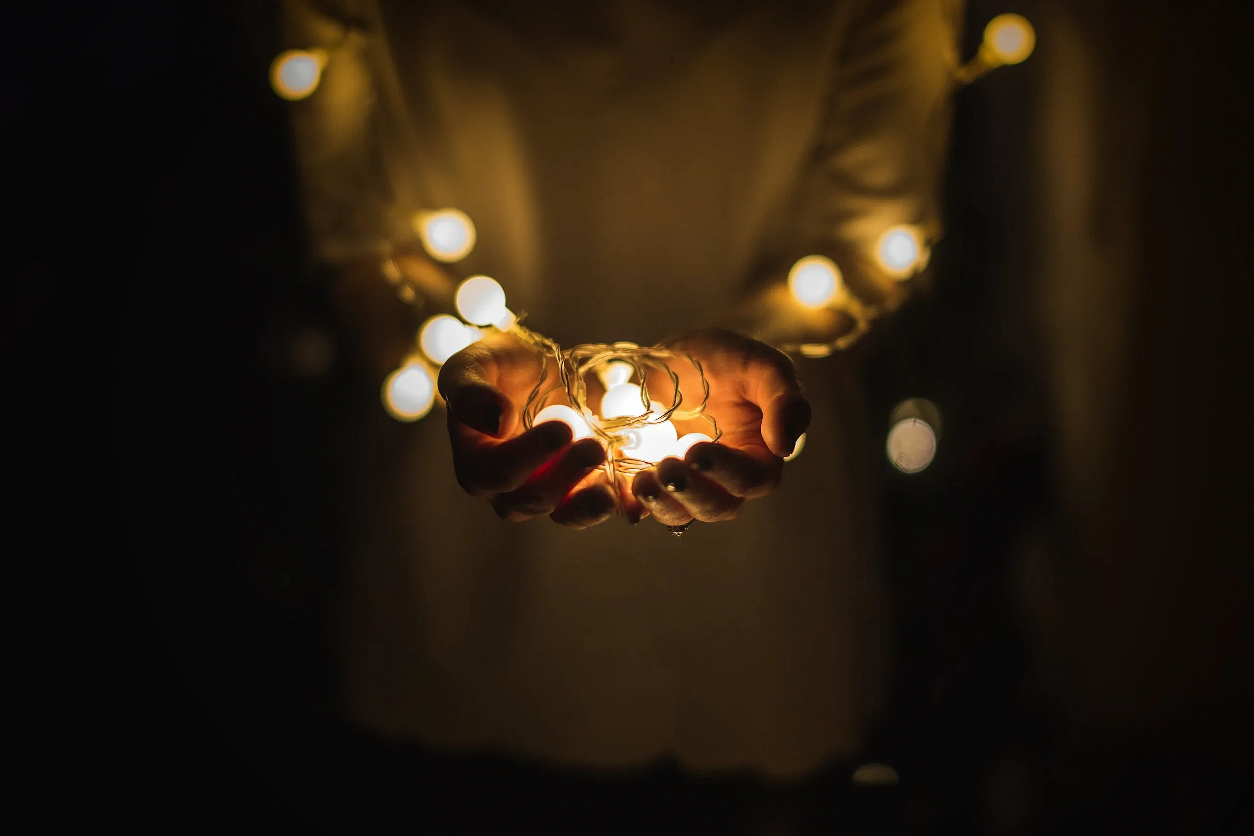 Hands gently holding glowing string lights in a dark setting.