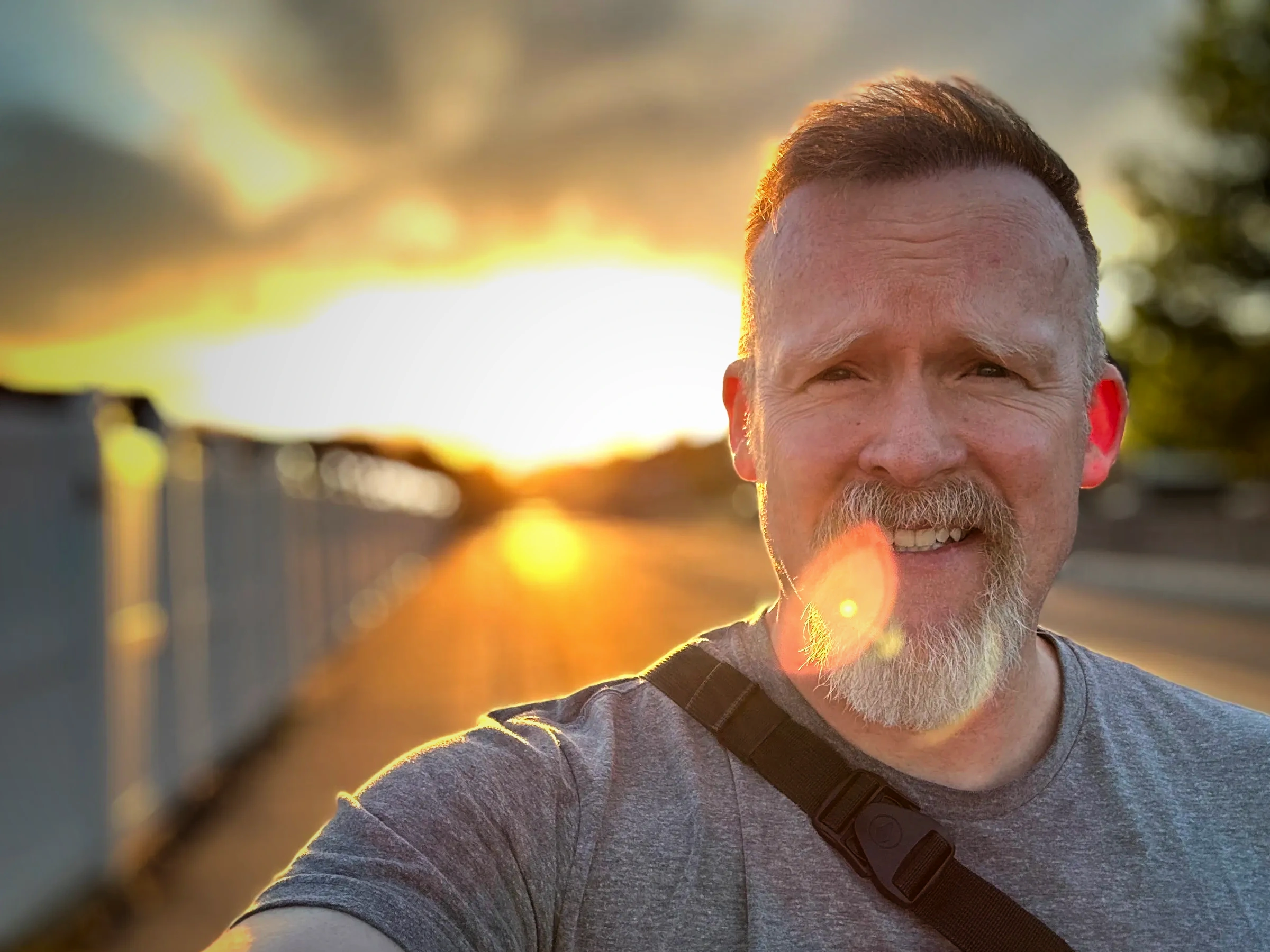 Smiling man with sunset background and shoulder strap.