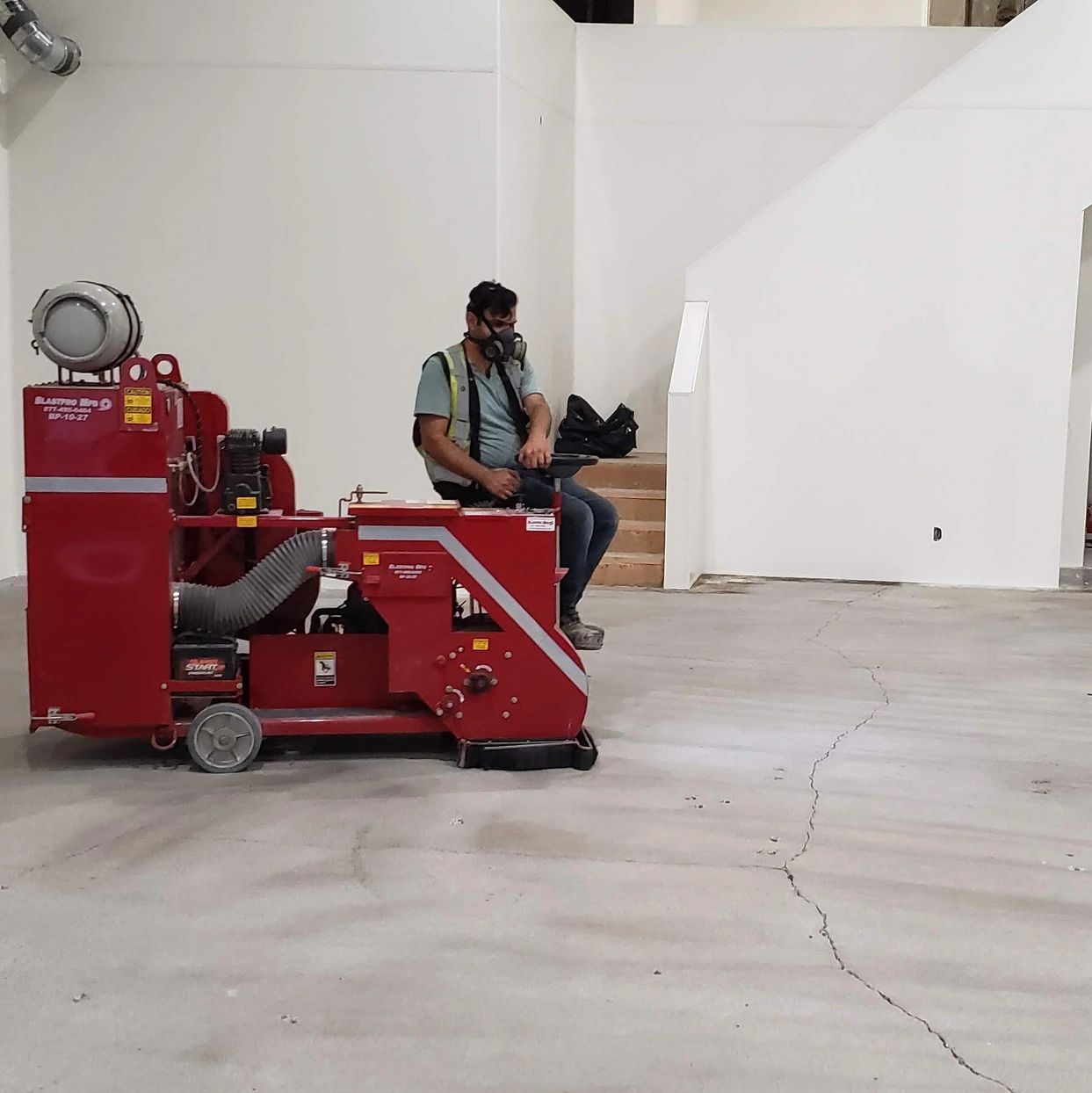 Worker using machinery on cracked concrete floor.