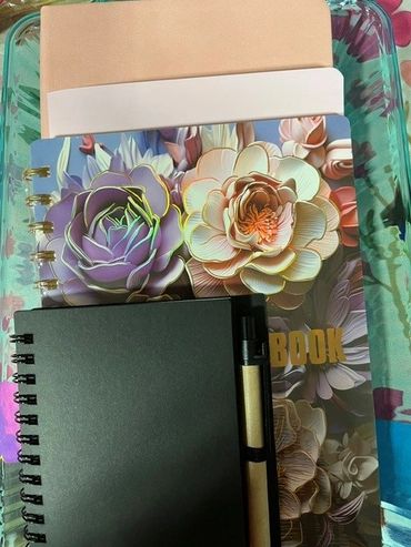 Stack of colorful and plain notebooks with a pen in a glass container.