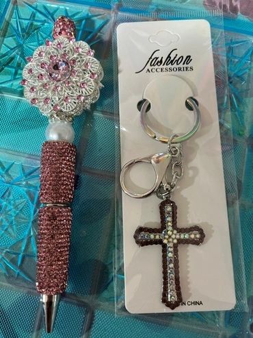 Decorative pen and jeweled cross keychain on a blue textured surface.