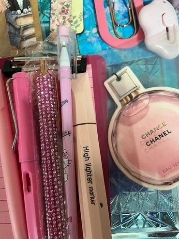 A collection of pink stationery items and a Chanel perfume notepad on a blue surface.