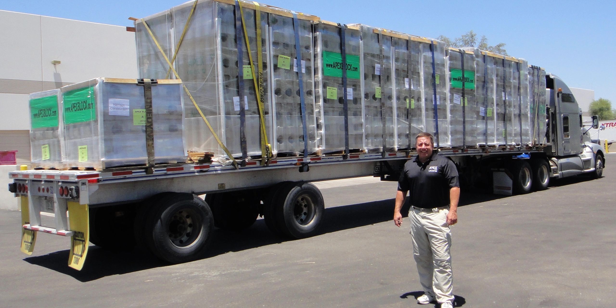 A man stands proudly beside a flatbed truck fully loaded with Apex Block products