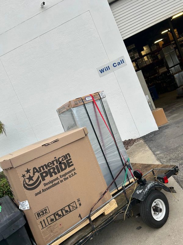 Large boxed appliance on a trailer outside a warehouse.