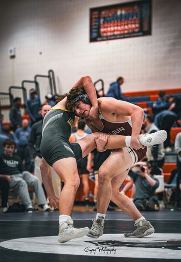 Two high school wrestlers intensely competing during a match in a gymnasium.