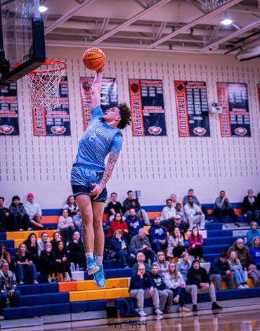 Basketball player in blue jersey mid-air for a dunk in a packed gym.
