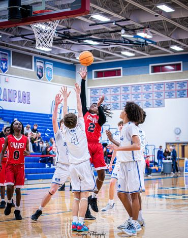 A basketball player in red jumps to score while surrounded by defenders in white.