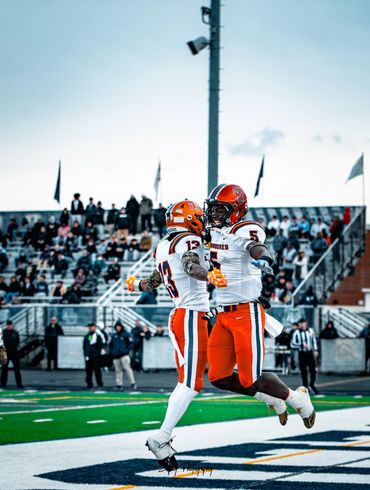 Two football players in orange and white uniforms celebrating on the field.