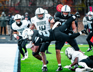 High-action football game with player diving near the sideline under heavy defense.