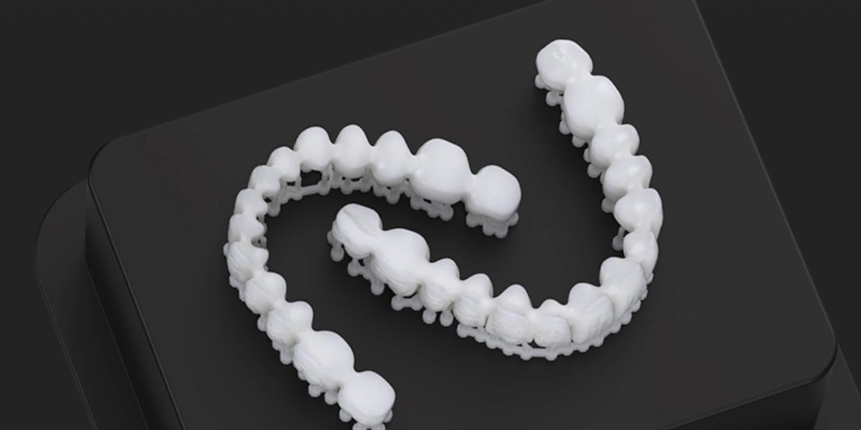 3D printed dental molds held on a black platform by a gloved hand.