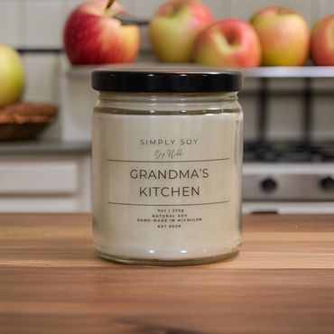 A natural soy wax jar candle sitting on a counter in a kitchen with fresh apples in the background.