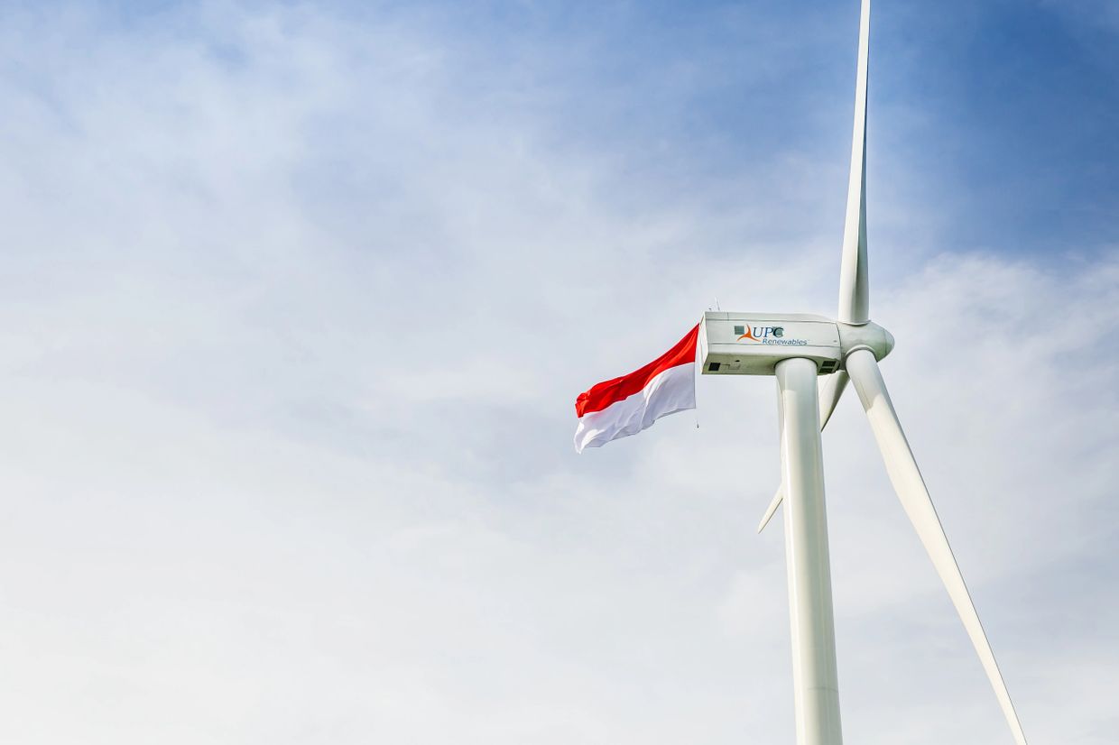 Wind turbine with a red and white flag against a blue sky.