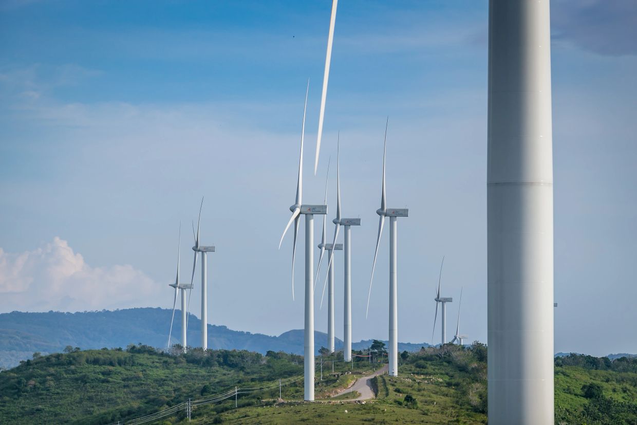 Wind turbines on a green hill under a clear blue sky.