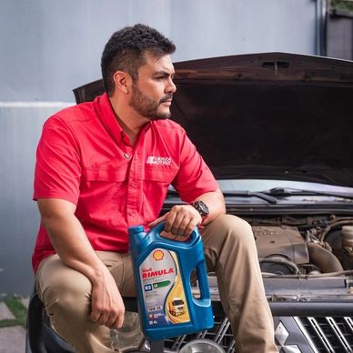 Mecánico sostiene aceite para motor junto a auto con capó abierto.