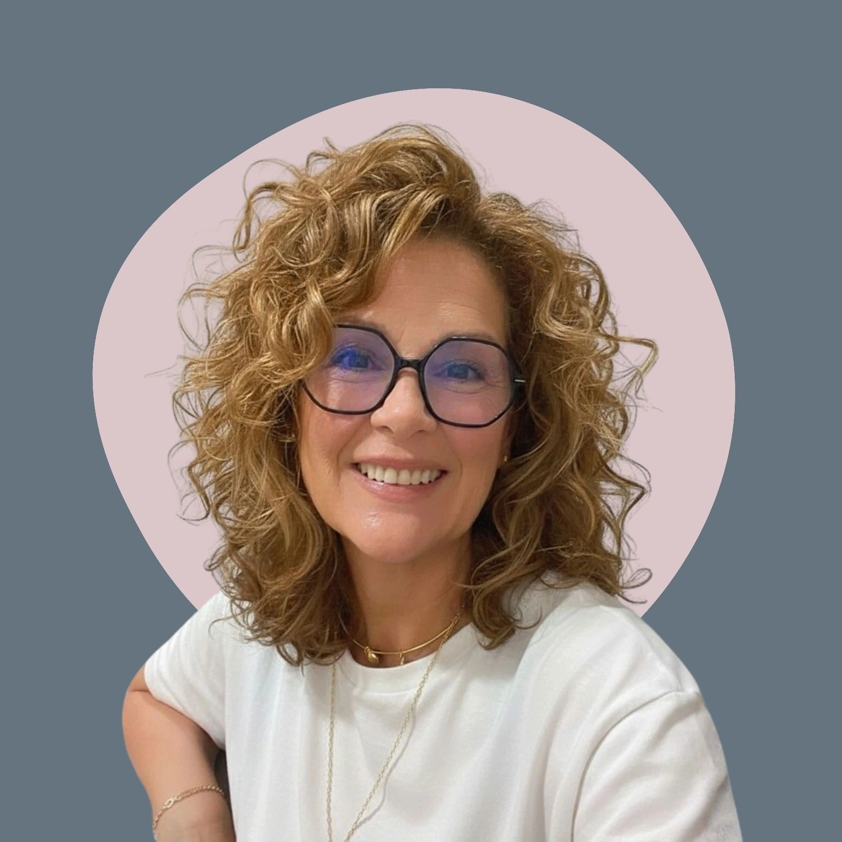 Smiling woman with curly hair and glasses against artistic background.