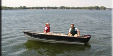 Two people in a small motorboat on a lake wearing life jackets.