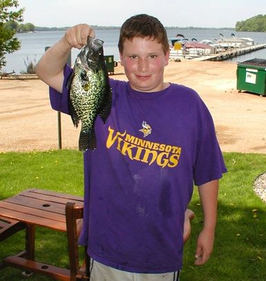 Boy holding a large fish by a lake dock.