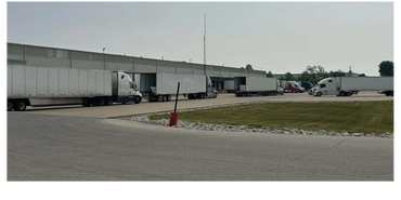 Several semi-trucks are parked at a loading dock of a large warehouse.