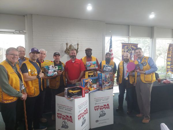 Group of men wearing Lions Club vests holding toys for a Toys for Tots donation drive.