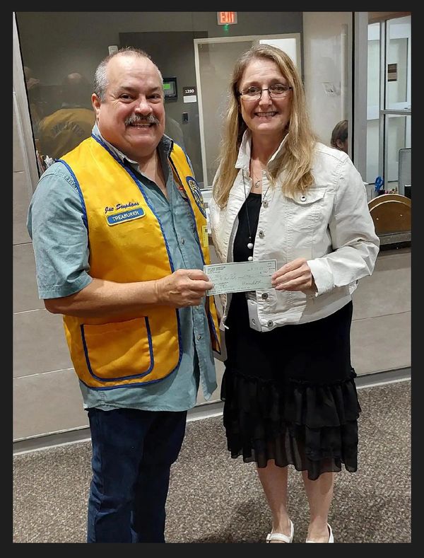 Man in yellow vest handing a check to a smiling woman in a white jacket.