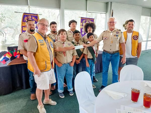 Boy Scouts and Lions Club members exchanging a check in a meeting room.