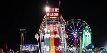Children ready to slide down a colorful carnival slide at night.
