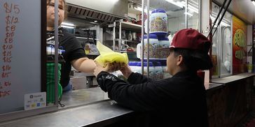 A person receives food wrapped in yellow paper at a food stand.