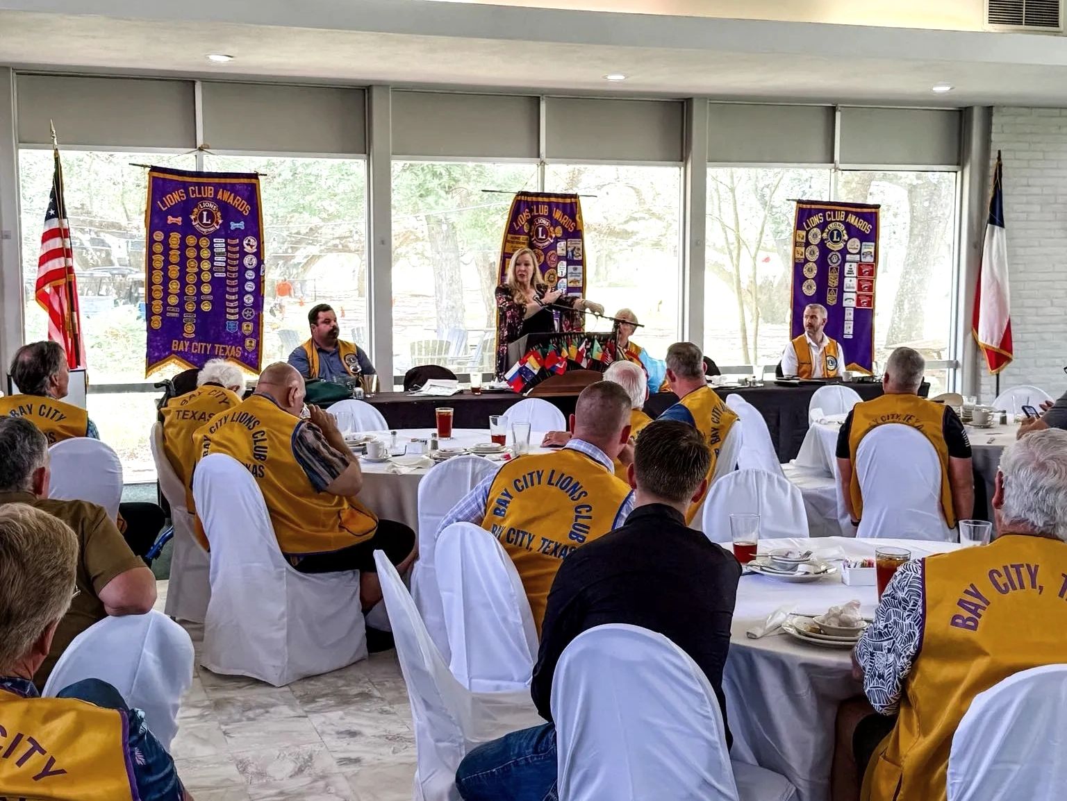 Bay City Lions Club meeting with speaker and members in yellow vests.