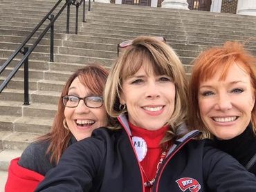 Three women smiling for a selfie on outdoor steps.