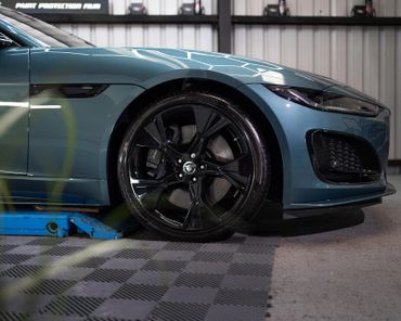 Close-up of a sleek blue sports car's front wheel and fender inside a garage.