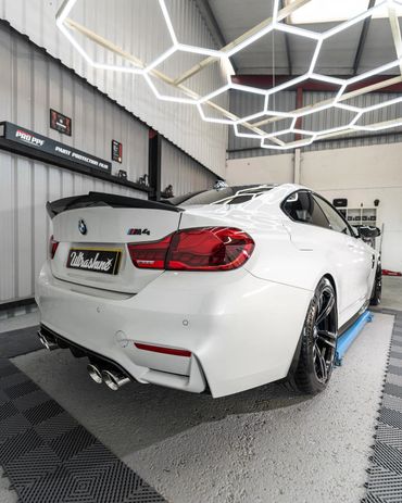Sleek white BMW M4 in a modern garage with hexagonal ceiling lights.